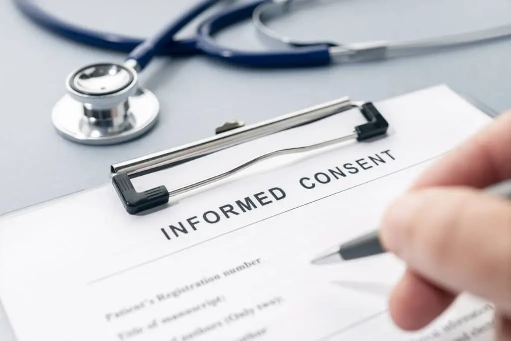 Hand filling a Informed Consent form and stethoscope on desk in reference to Law 25