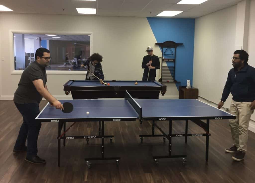 A group of people playing ping pong in an office.