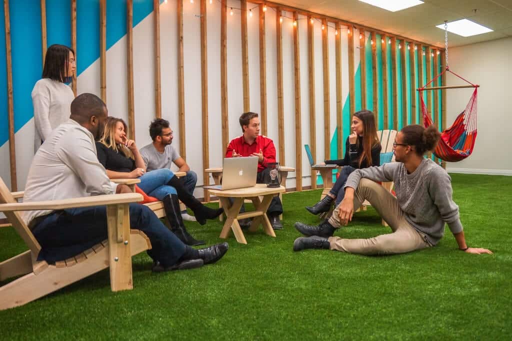 A group of people sitting on chairs in an office with artificial grass.
