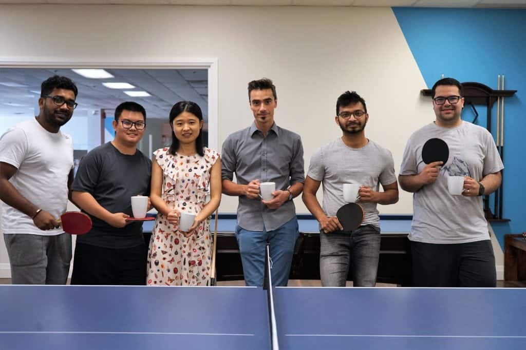 A group of people standing next to a ping pong table.