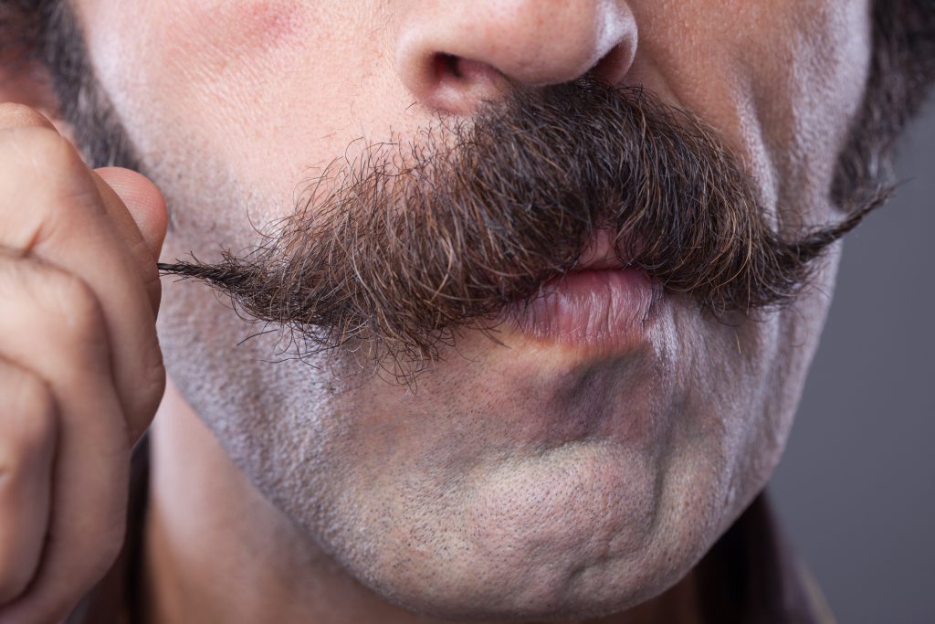 A man twisting the corner of his large moustache.