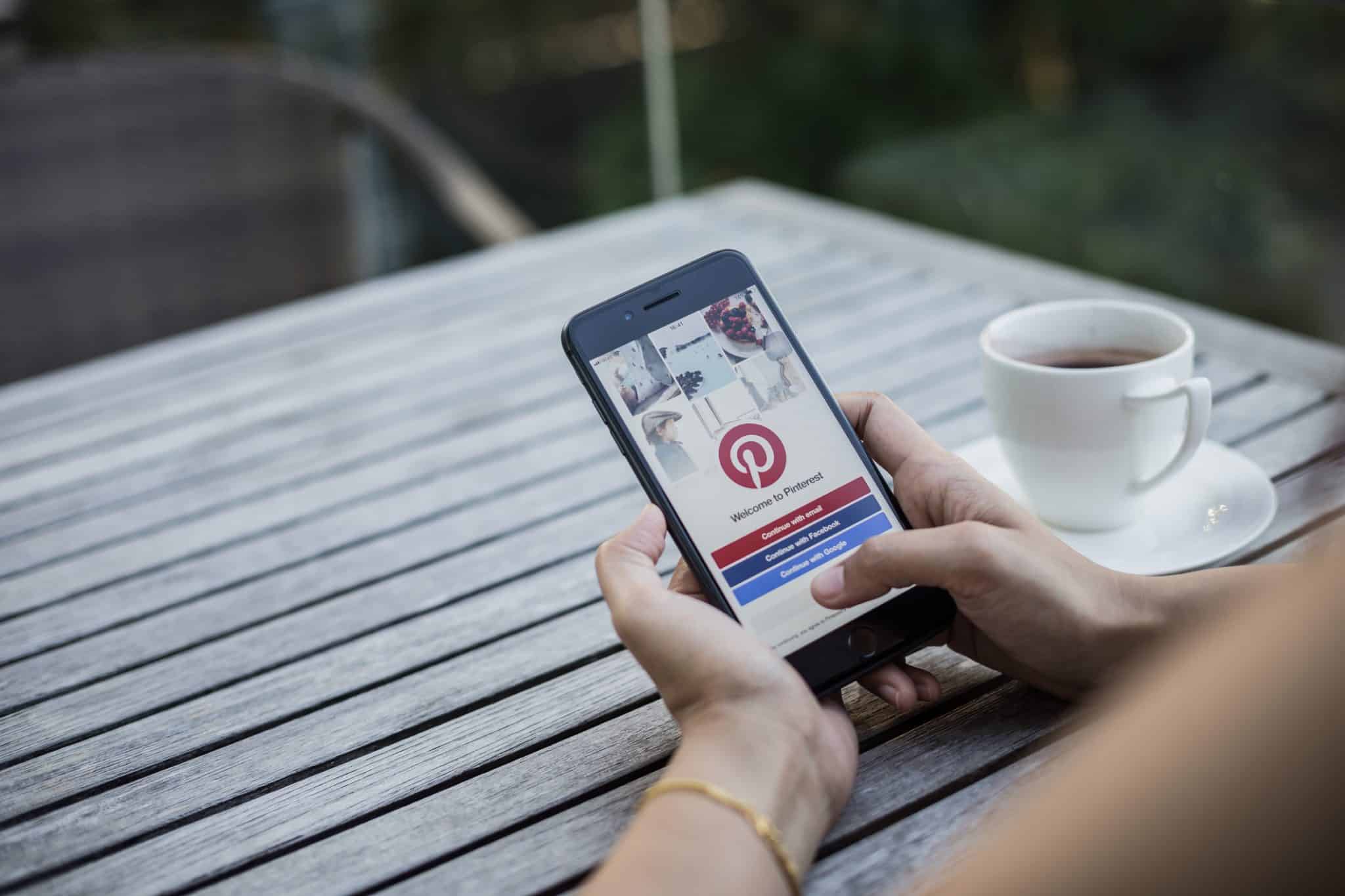 A woman employing a smartphone with the Pinterest logo on it for her marketing strategy.