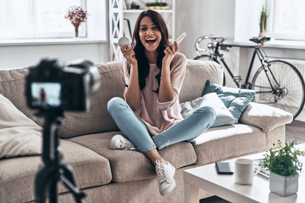 Young woman holding beauty products and smiling while making social media video