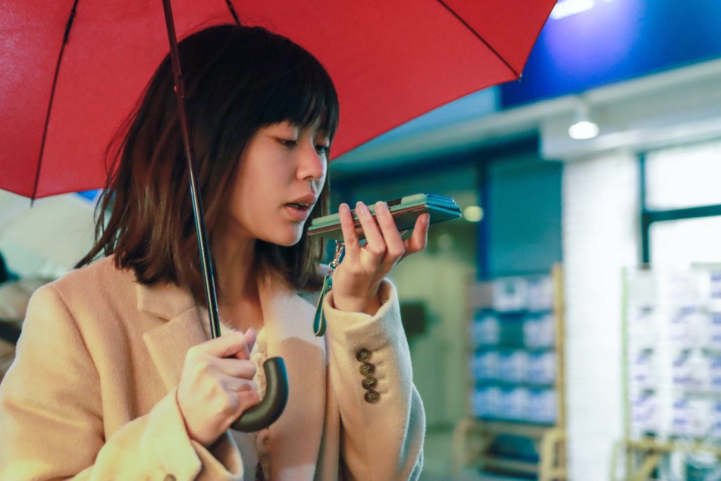 Young woman using voice search on the phone in the rain 