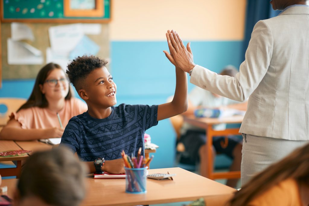 Happy schoolboy giving high-five to his teacher during class