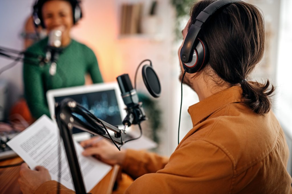 Back view of a young man recording a podcast on an interview with women in studio holding paper