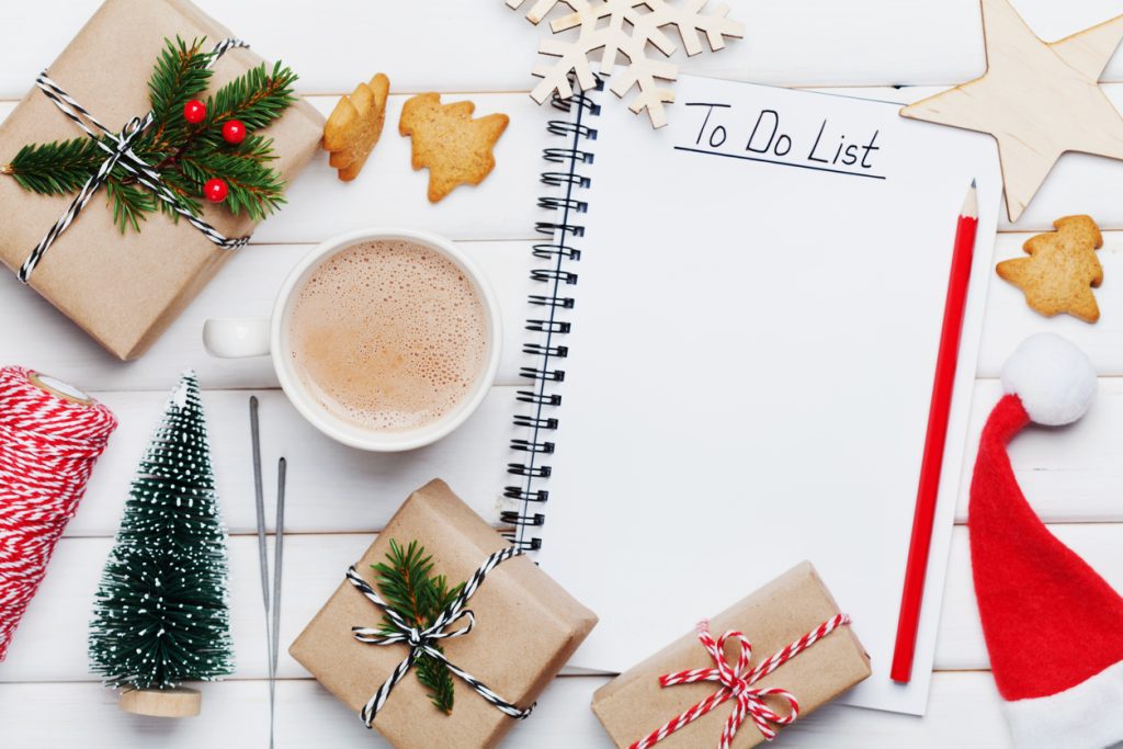 Cup of hot cocoa, holiday decorations, gift, present, miniature fir tree and notebook with eCommerce to do list on white wooden table.