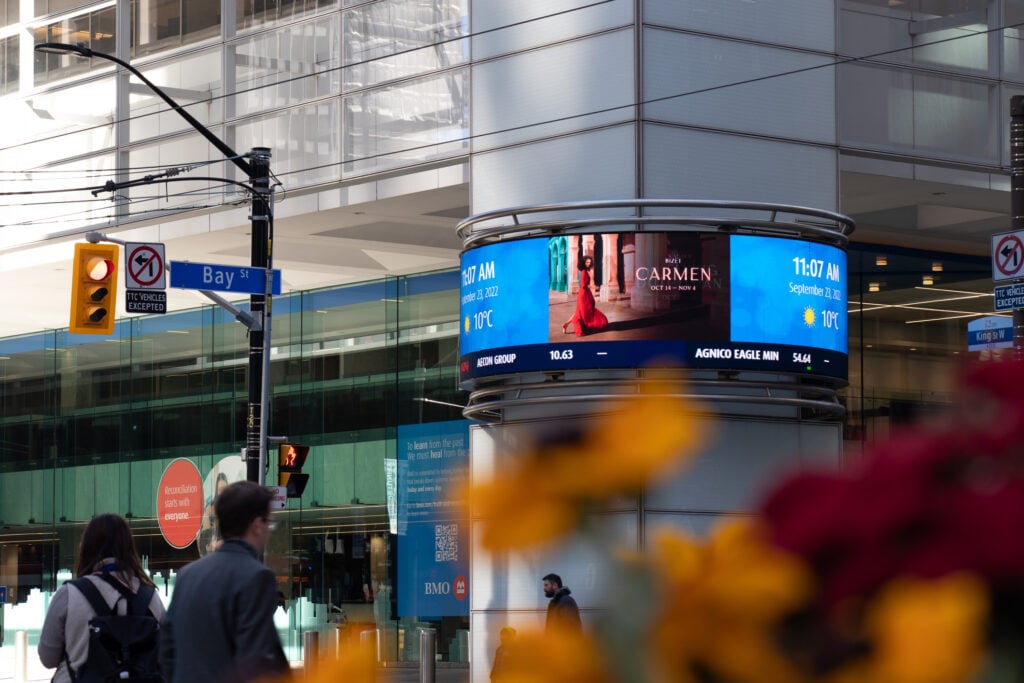 Digital billboard in downtown Toronto with pedestrians walking about.