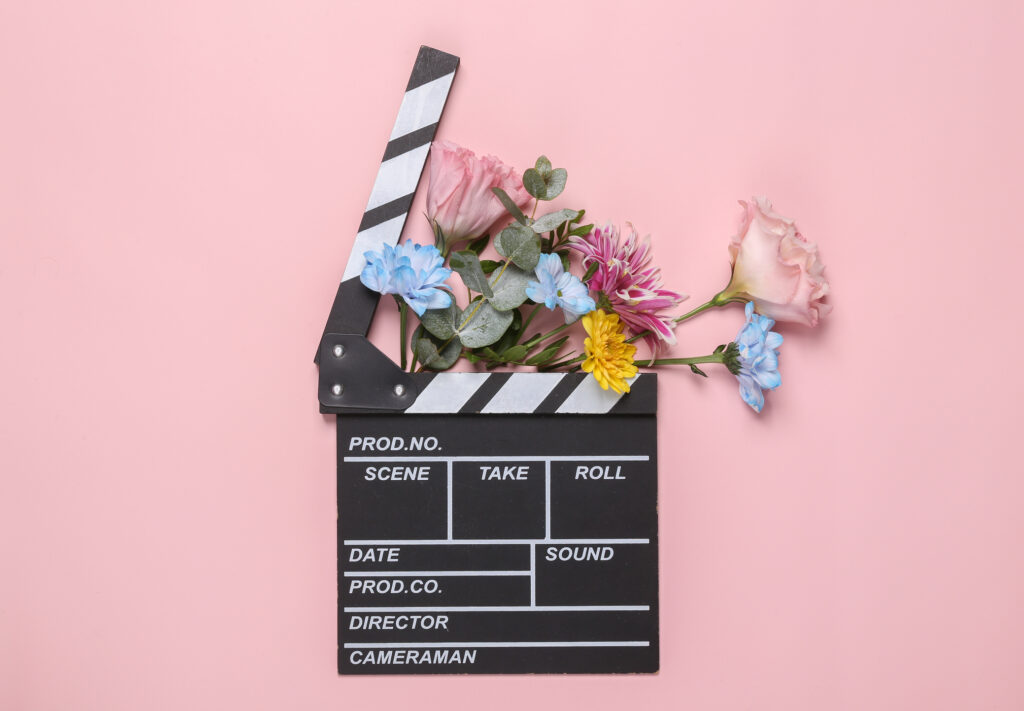 Director clapper board on a pink background surrounded by flowers. 