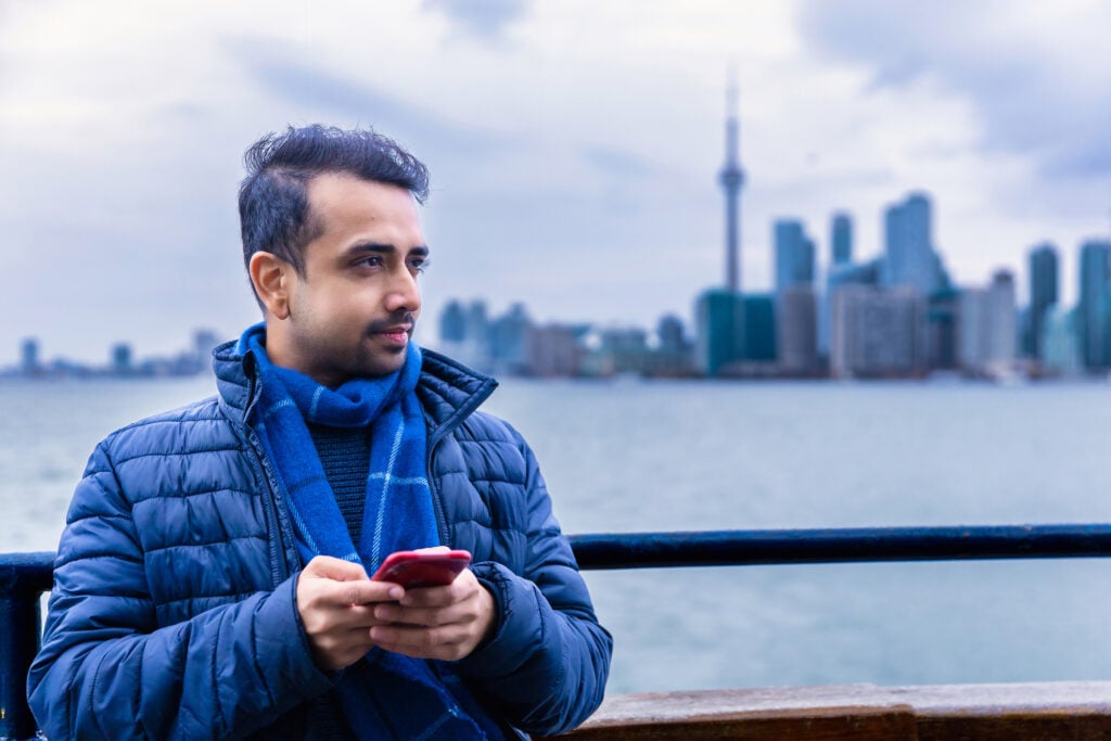 Man holding smartphone with Toronto skyline behind him. 