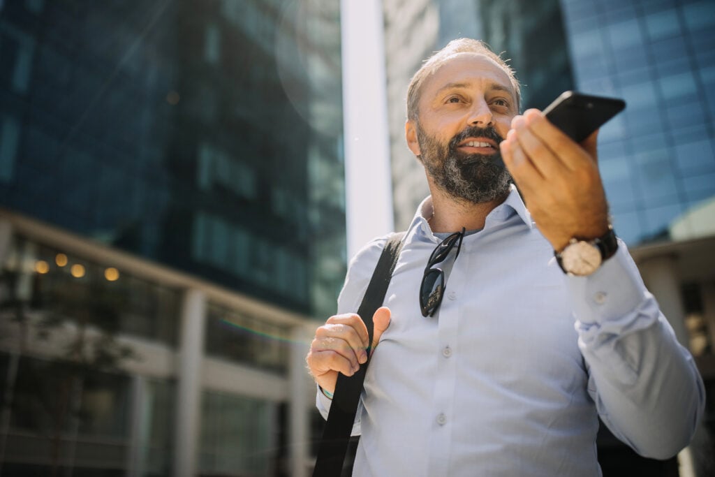 Businessman utilizing one of the leading digital trends, voice search on the sidewalk