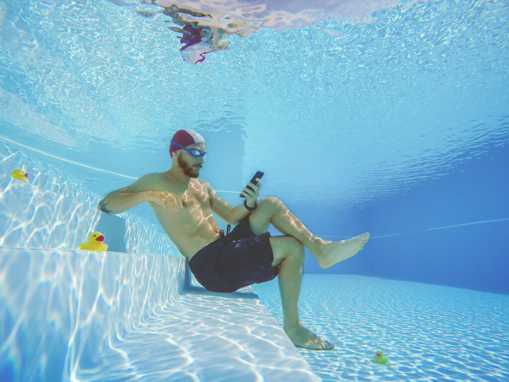 Man on the phone in the pool, underwater reviewing digital marketing campaign