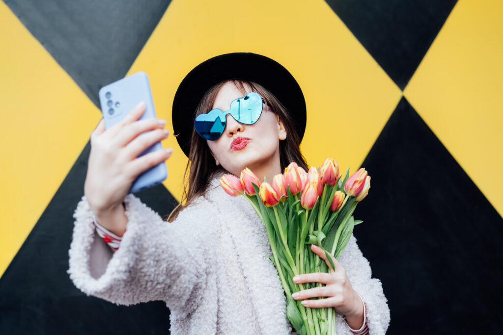 Social media influencer holding tulips and taking selfies in front of a wall for a digital marketing campaign. 