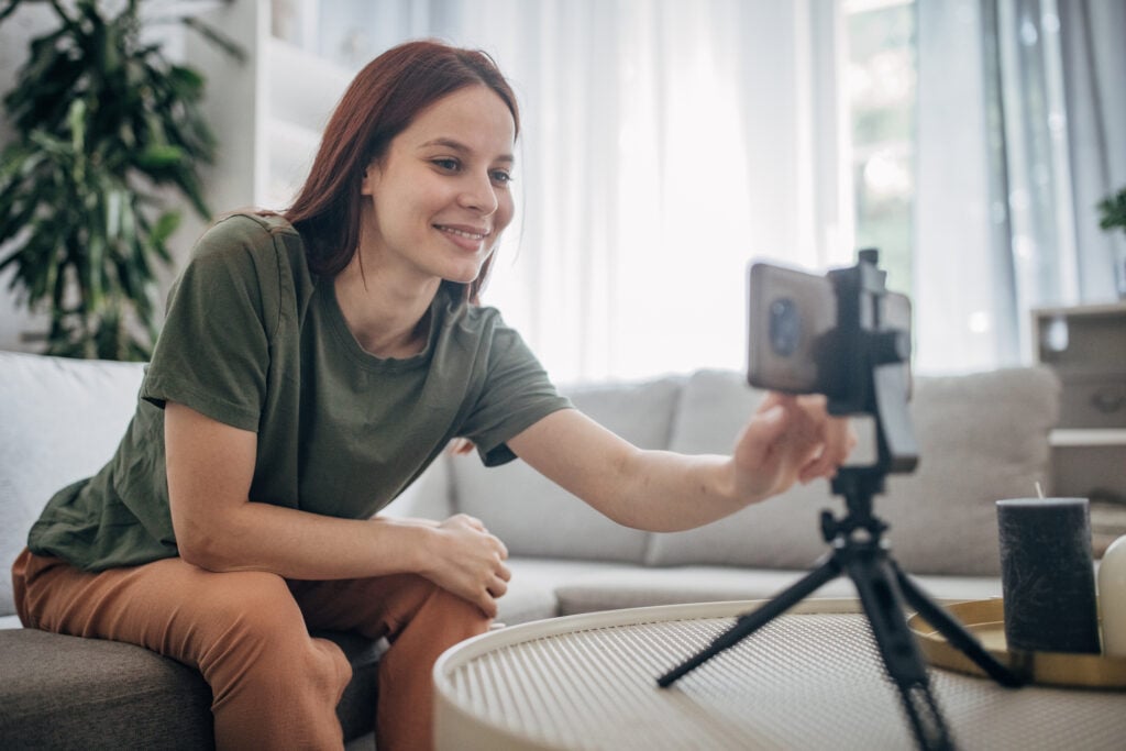 Woman using smartphone to film her blog while sitting on her sofa working at home for a digital marketing agency