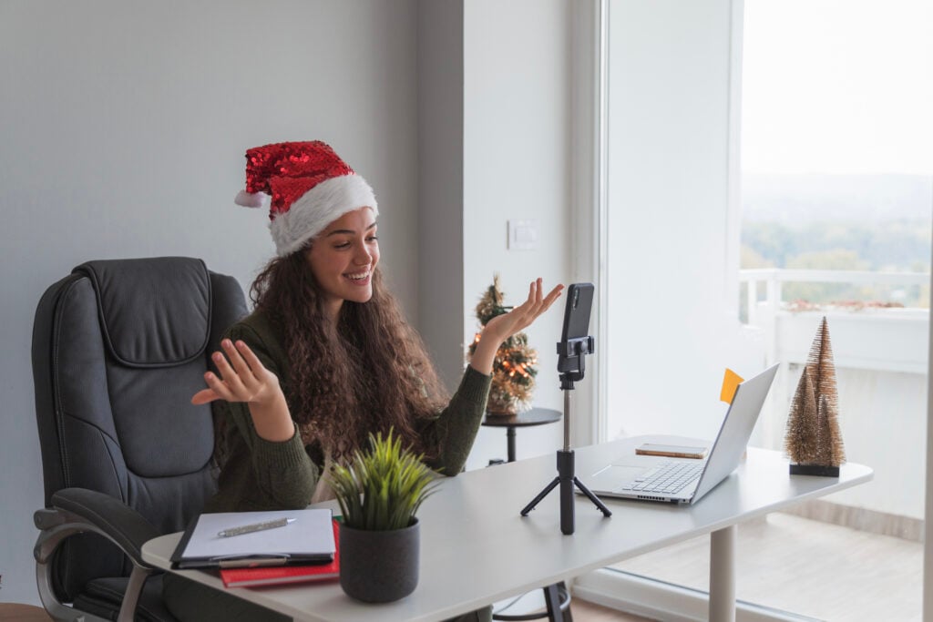 Happy female influencer filming social media marketing trends content and wearing Santa hat during winter holidays 