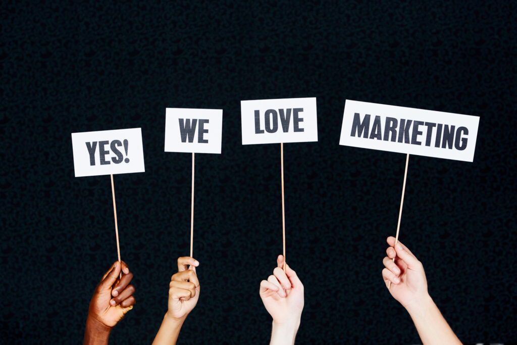 Four hands holding up four signs that read “Yes! We love marketing.” in reference to love for a digital marketing agency. 