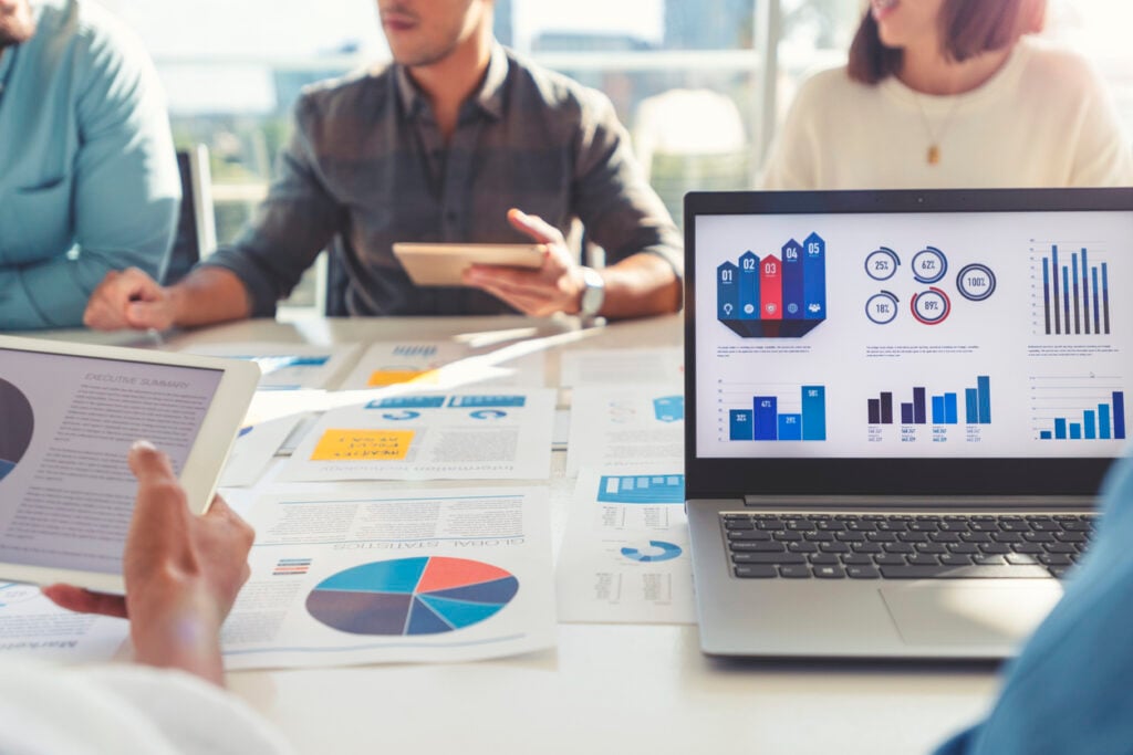 Close-up of digital advertising metrics displayed on a laptop screen, with team members analyzing charts, graphs and performance data during a strategy meeting.