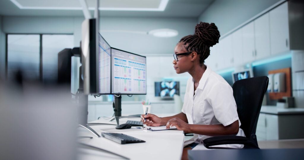 A healthcare professional analyzing digital data on multiple monitors, symbolizing the importance of expertise and trust in pharma SEO.
