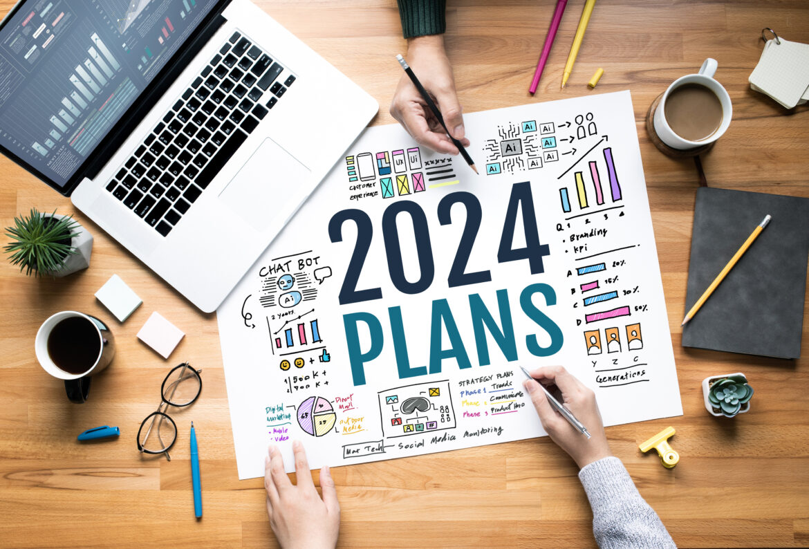Two people working at a desk with a 2024 plan surrounded by icons and graphics.