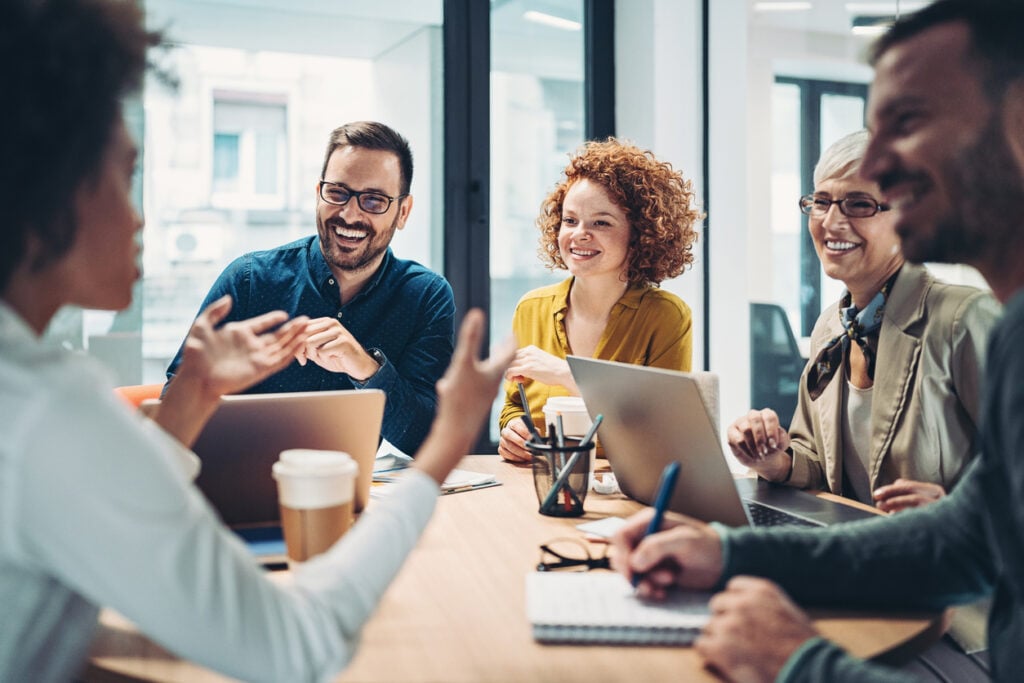 Diverse marketing team collaborating at a table with laptops and coffee, brainstorming creative ideas for a digital advertising campaign in a modern office.