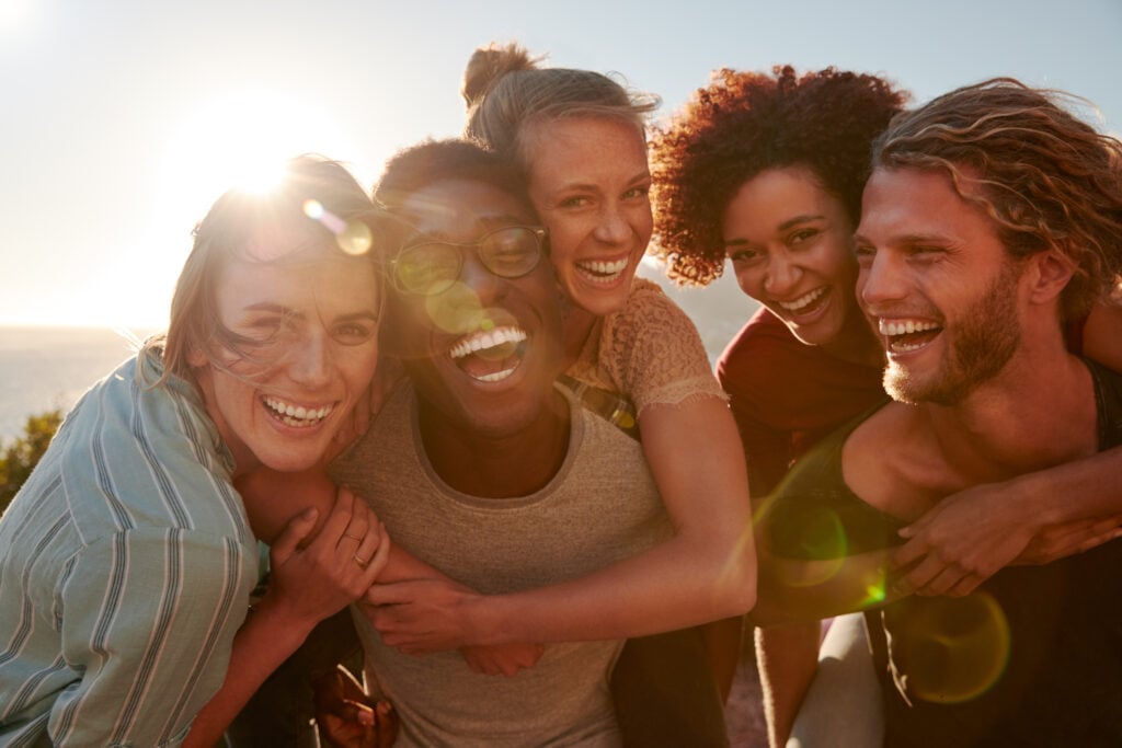 Group of young adults laughing and hugging at sunset, capturing the playful and joyful spirit of April Fools’ Day.