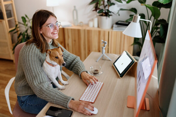 Gen Z woman sitting at a desk on a computer with her dog.