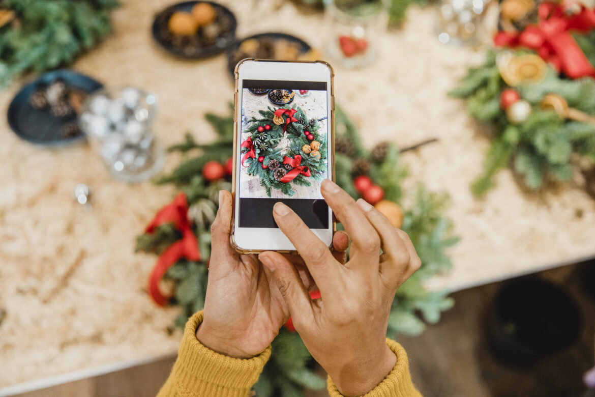 Woman taking a picture of a festive wreath for holiday marketing campaigns.