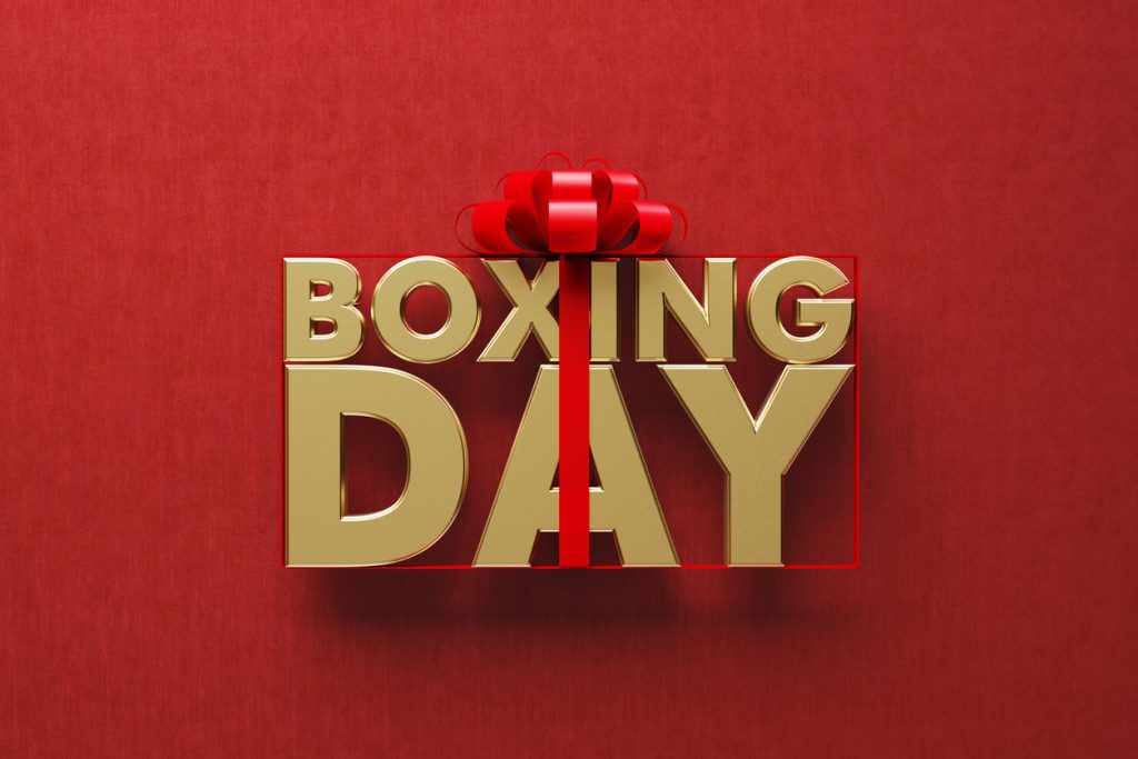 Gold coloured Boxing Day word wrapped by red ribbon on red background.